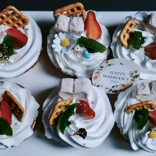 Six white mallow cupcakes topped with strawberries, marshmallows, and pretzels, one has a "Happy Woman's Day" tag.