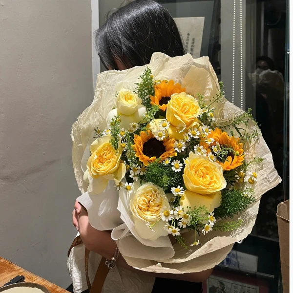 Yellow roses and sunflowers in a bouquet, held by a person.