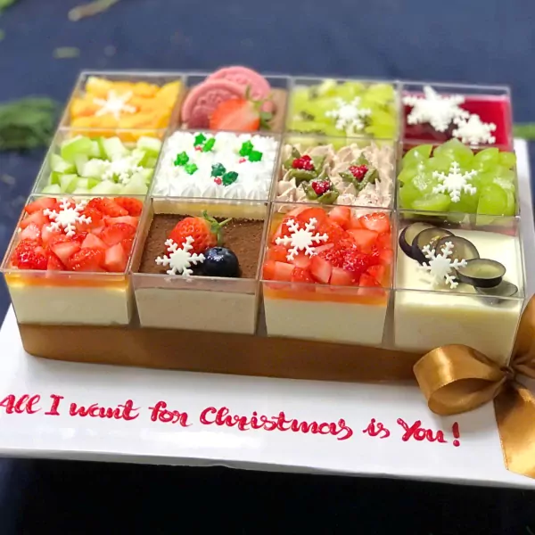 Nine Christmas mousse desserts in clear cups with fruit and snowflake decorations, on a platter with "All I want for Christmas is You!" written.