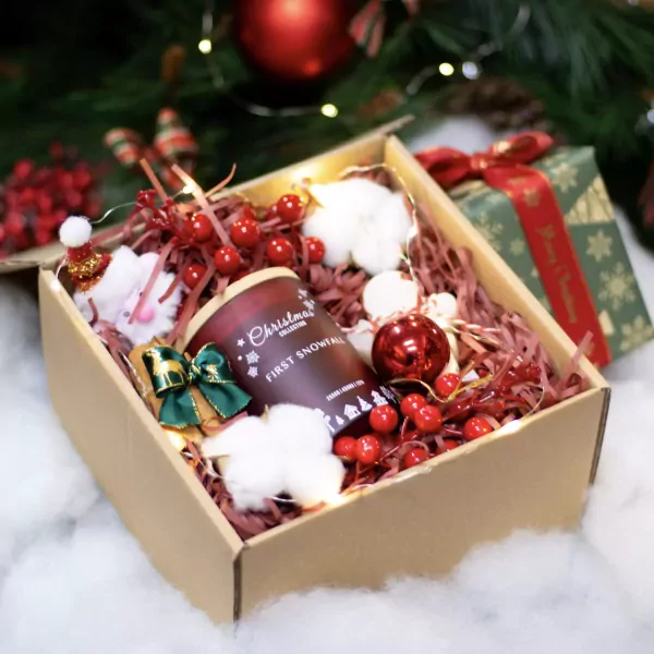 A Christmas gift box filled with a candle, ornaments, and festive decorations.