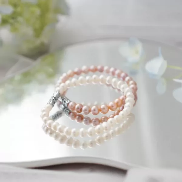 Three delicate pearl bracelets in white, pink, and peach colors, reflecting on a mirrored surface.