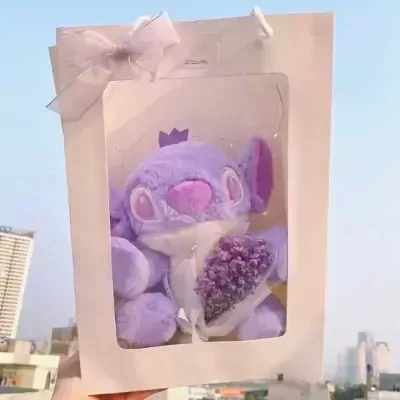 Purple Stitch plush toy with a crown, holding a mini bouquet of purple flowers in a white gift box with a ribbon.