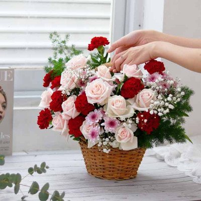 A woven basket overflowing with pink roses, red carnations, and baby's breath.