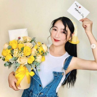 Woman in denim overalls holding a yellow rose bouquet and a Mother's Day card.