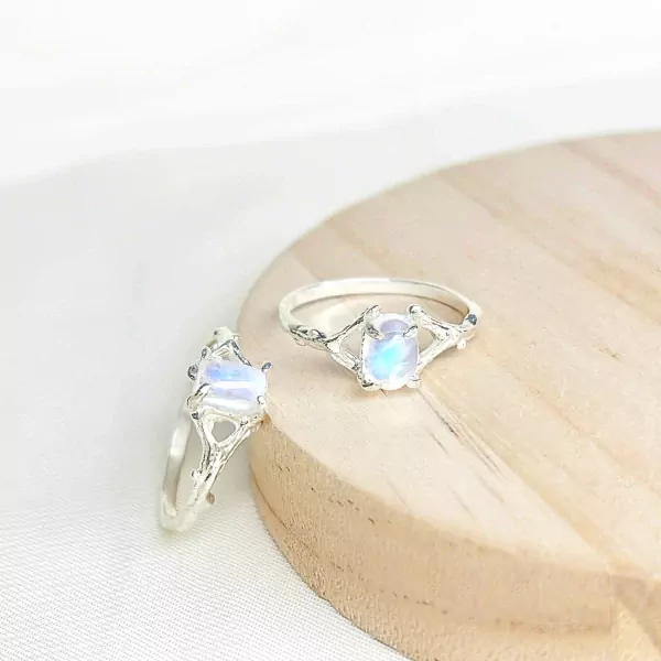 Two silver rings with oval moonstones, one in front and one behind, on a wooden surface.