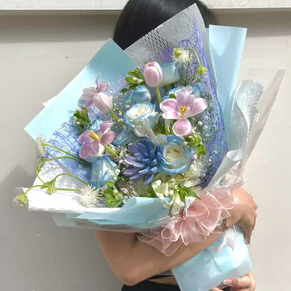Bouquet of pink tulips, blue roses, succulents, and orchids in pastel blue and pink wrapping.