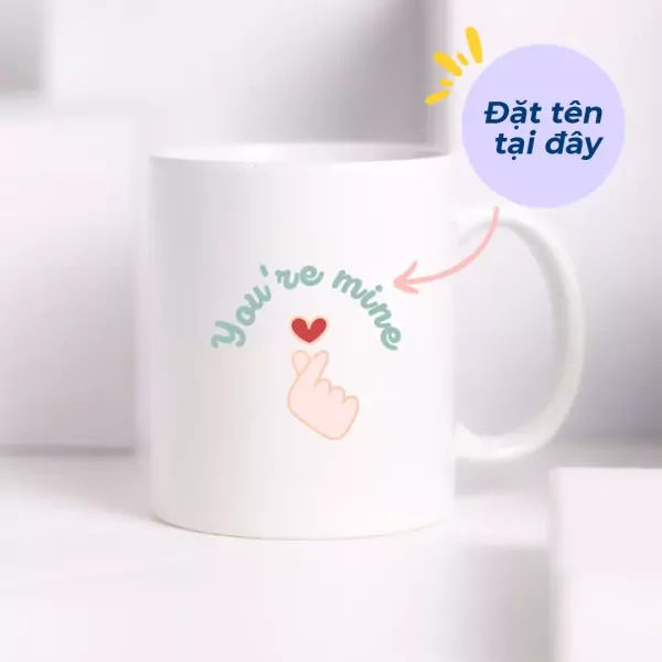 White ceramic mug with "You're mine" text and finger heart design.