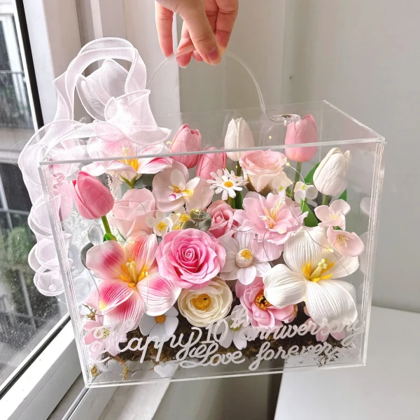 A clear acrylic box filled with pink and white artificial flowers, a white ribbon, and "Happy 10th Anniversary Love Forever" inscribed on the front.