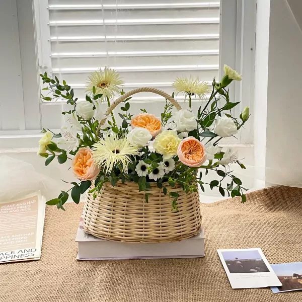A woven basket overflowing with peach, white, and yellow roses, carnations, and other greenery.