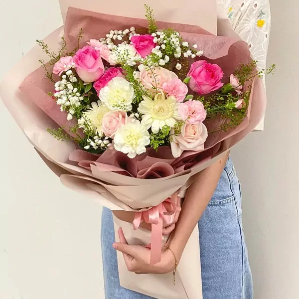 Bouquet of pink and white roses, daisies, carnations, and baby's breath in brown and pink wrapping.