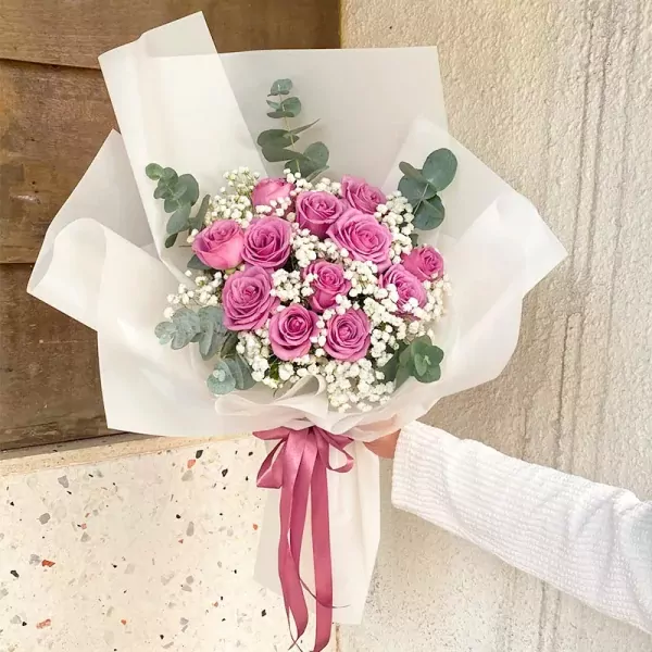 Pink roses and baby's breath bouquet wrapped in white paper with a pink ribbon.