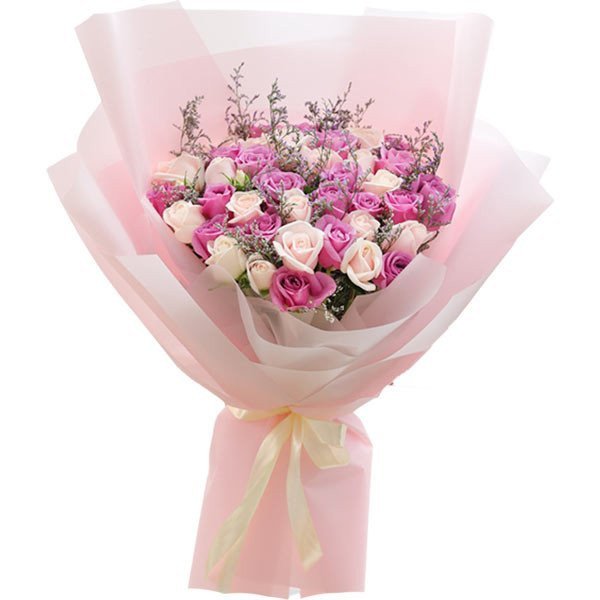 Bouquet of pink and lavender roses with delicate filler flowers, wrapped in pink paper and tied with a light yellow ribbon.