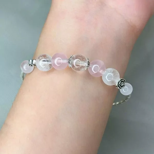 A delicate bracelet with rose quartz, clear quartz beads, and silver charms on a wrist.