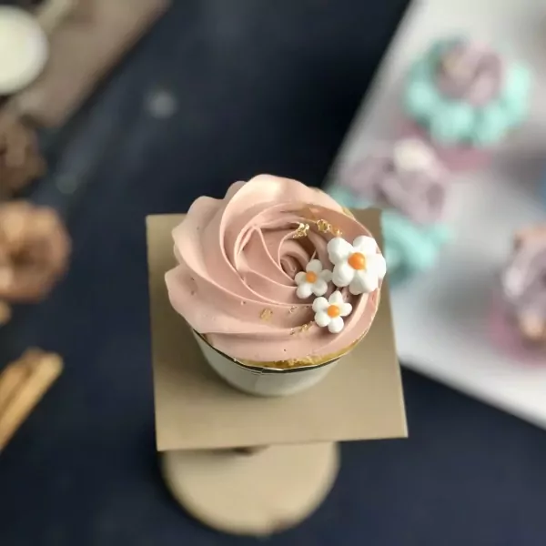Pink rose cupcake with white flowers and gold flakes, on a stand.