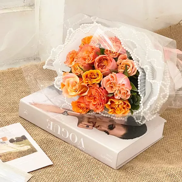 Orange and pink roses in a bouquet on a Vogue book.