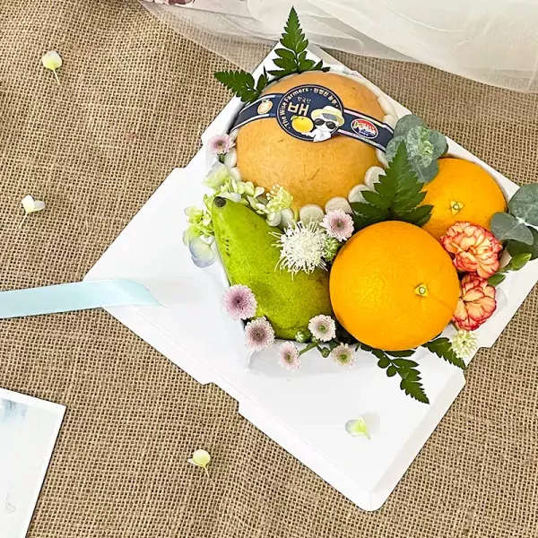 A sweet fruit box with pears, oranges, flowers, and leaves on a burlap background.