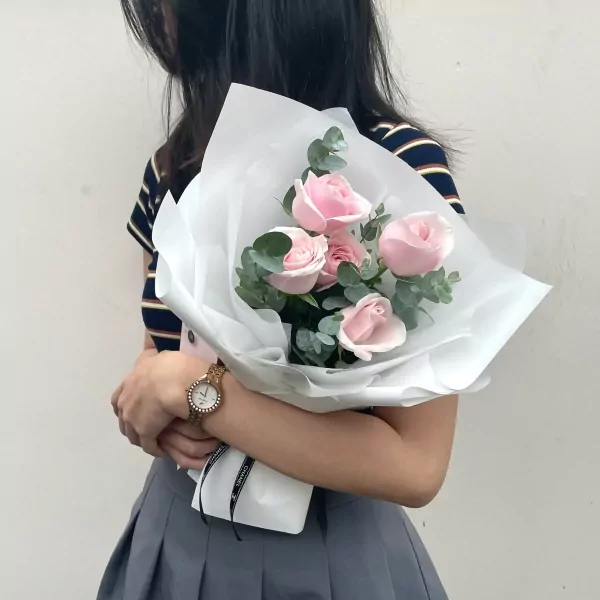 A bouquet of pink roses and eucalyptus wrapped in white paper.