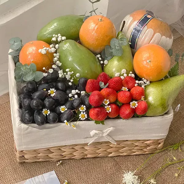Fruit basket with mangoes, pears, oranges, strawberries, grapes, and small white flowers.