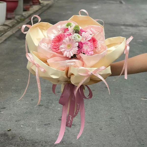 Pink and cream flowers with satin ribbons arranged in a bouquet.