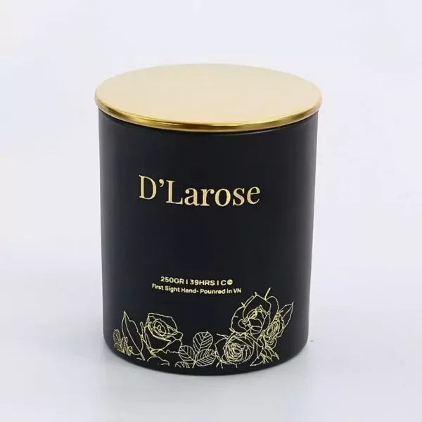 Black scented candle with gold lid and floral accents, "D'Larose" label.