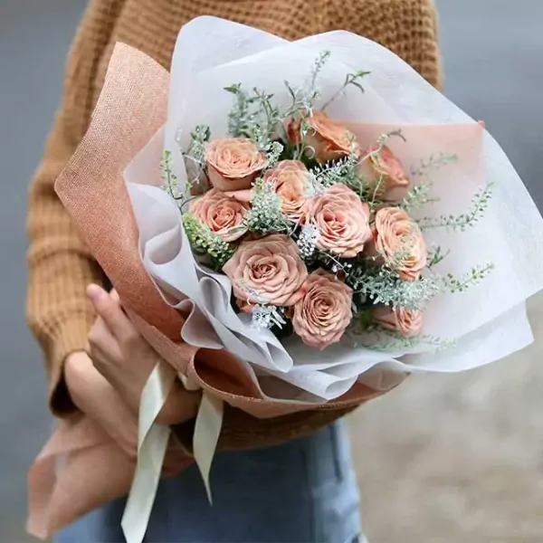 Peach roses bouquet wrapped in brown and white paper with a ribbon.