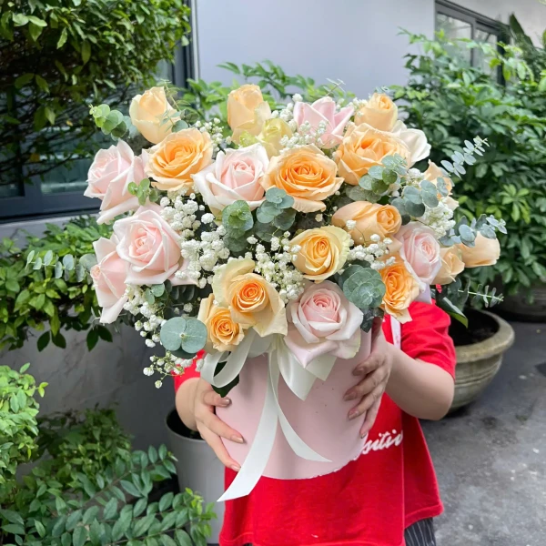 Pink and peach roses with baby's breath in a pink box, held by a person in a red shirt.