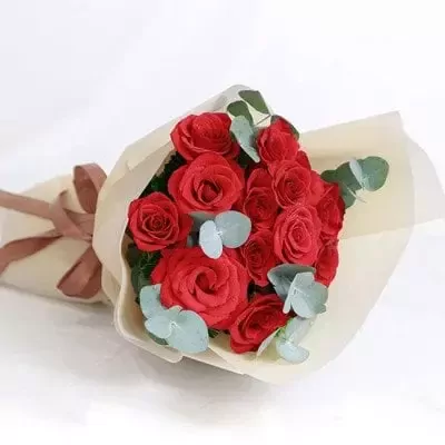 Bouquet of 12 red roses with eucalyptus leaves, wrapped in cream paper and tied with a brown ribbon.