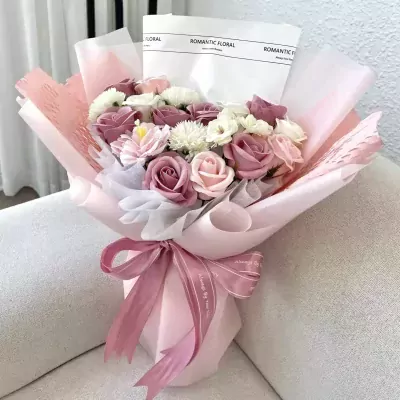A bouquet of pink and white roses and other flowers, wrapped in pink and white paper with a pink ribbon.
