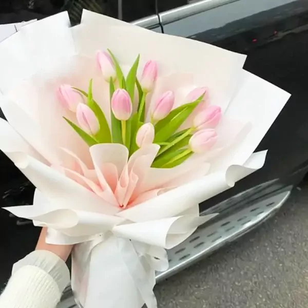 Pink tulips in a white and pink bouquet with a person holding it.