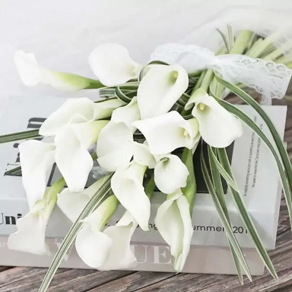 White calla lily bouquet tied with lace ribbon, resting on books.