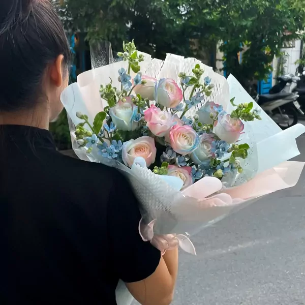 A woman holds a bouquet of pink and blue ombre roses with small blue flowers.