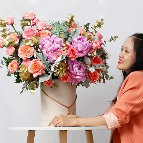 A woman smiles at a large pink and orange floral arrangement in a white box.