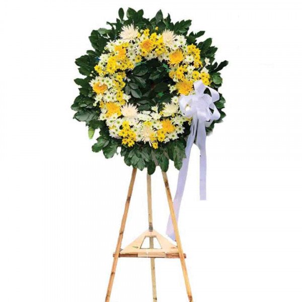 Wreath of yellow and white flowers on a wooden stand with a white ribbon.