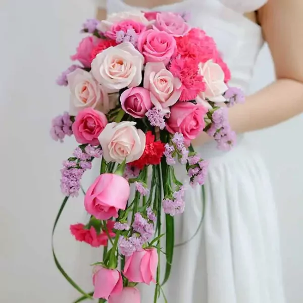 Cascading wedding bouquet of pink and cream roses, carnations, and lavender statice.