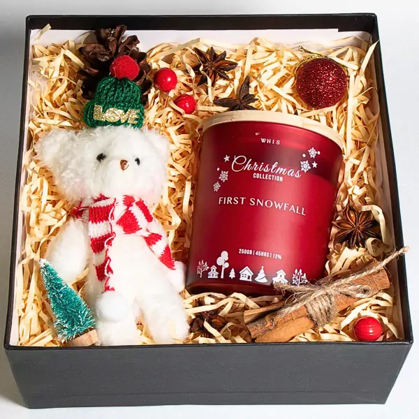 Christmas gift box with a teddy bear, candle, cinnamon, and pinecone.