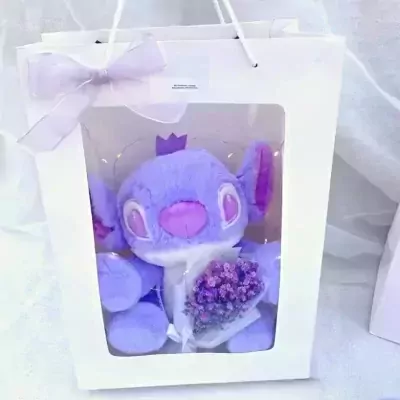 Purple Stitch plush toy with a crown and a bouquet of mini flowers in a white gift bag.