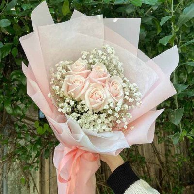 Bouquet of pink roses and baby's breath wrapped in light pink paper.