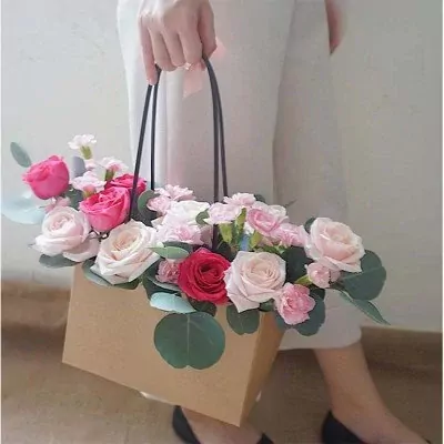 Hand holding a floral arrangement in a brown box with roses and carnations.