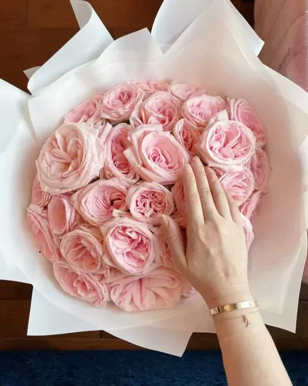 Bouquet of light pink roses with a woman's hand touching them.