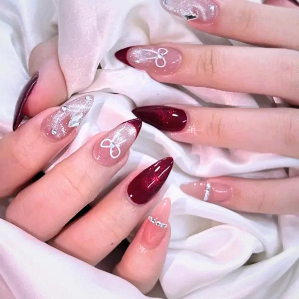 Woman's hands with long, almond-shaped nails in deep red and glittery designs.