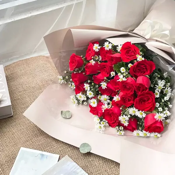 Bouquet of red roses and white daisies in elegant wrapping.