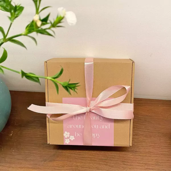 A brown gift box with pink ribbon and a pink label saying "the beauty around you and be happy".