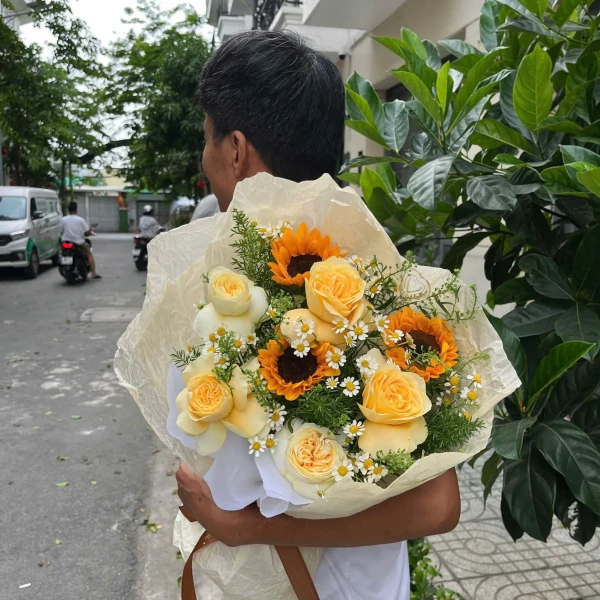 Man holding a bouquet of sunflowers, yellow roses, and daisy-like flowers.