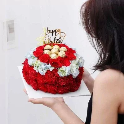 Round red flower cake with Ferrero Rocher chocolates and a "Happy Birthday" topper, held by a woman.