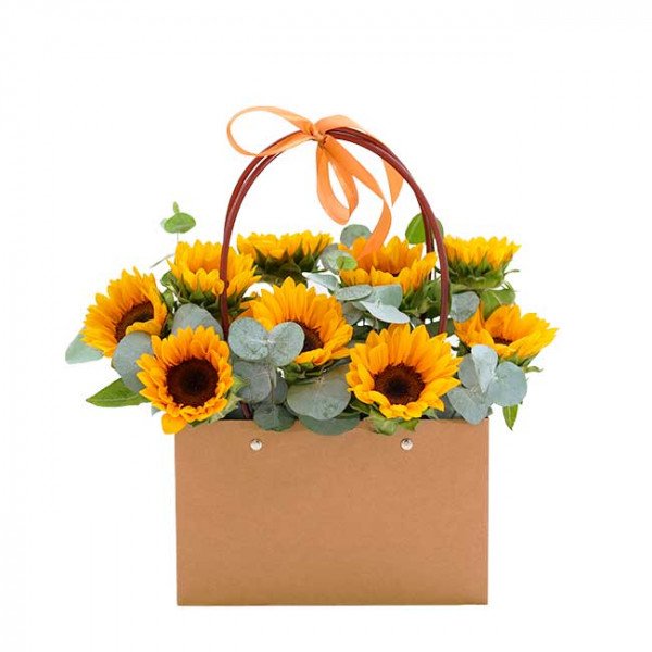 A brown paper flower bag filled with sunflowers and eucalyptus leaves, tied with an orange ribbon.