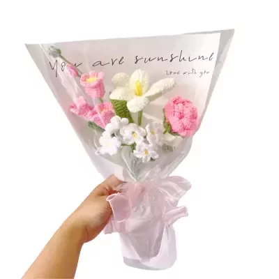 Crocheted bouquet of pink and white flowers wrapped in translucent paper, held by a hand.