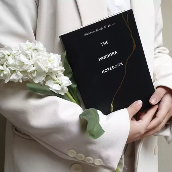 A black notebook with gold lettering "THE PANDORA NOTEBOOK" held by hands.