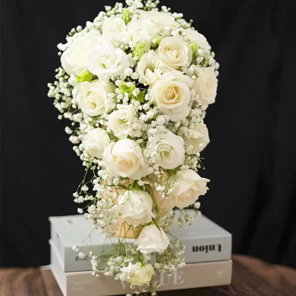 Cascading bouquet of white roses and baby's breath, presented in a vase on top of books.