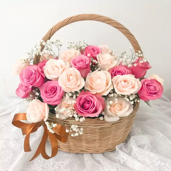 Basket of pink and cream roses with baby's breath, tied with a bronze ribbon.