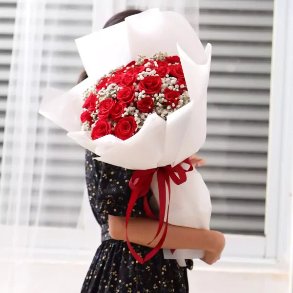 A bouquet of red roses and baby's breath, wrapped in white paper and tied with a red ribbon.
